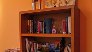 Ein Holzbücherregal mit Büchern, eine Vase mit Trockenpflanzen und ein Blumenbild an der Wand.
