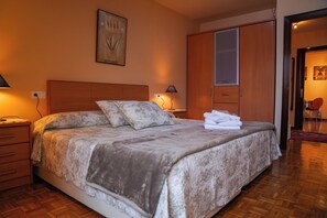 Een slaapkamer met een groot bed, een houten garderobe en een nachtkastje met een lamp.