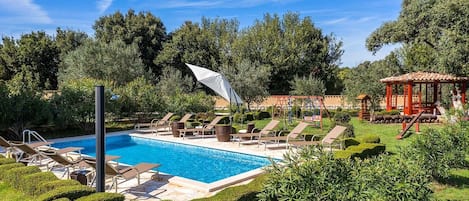 En swimmingpool med liggestole og en pavillon i en anlagt have.