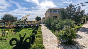 A well-maintained garden with a stone pathway, a children's play area, and a building with a tiled roof. - Villa Divina in Sisan (Sisan)