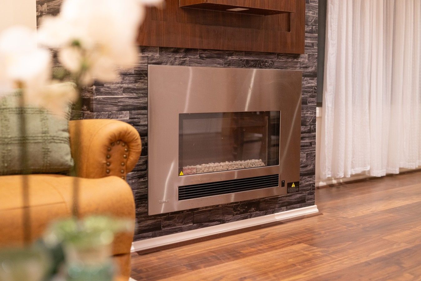 Ein moderner Kamin mit Steinverkleidung, ein Holzschrank darüber und ein gepolsterter Sessel links.