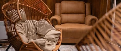 A room with a wicker chair, a brown sofa, and a patterned rug.