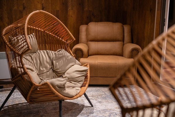 Una habitación con una silla de mimbre, un sofá marrón y un tapete estampado.