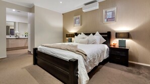 A bedroom with a large bed, bedside lamps, a flat-screen TV, and a built-in air conditioning unit. - Modern Cozy Retreat, Park, Mall! (Berwick)