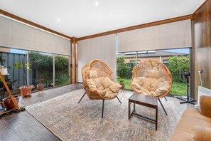 A spacious room with large windows, two wicker chairs, a small table, and a potted plant. - Spacious 4BR Family Retreat | Theatre & Sunroom (Berwick)