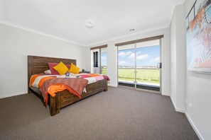 A bedroom with a large bed, a view of a green field through a sliding door, and a painting of tigers on the wall. - Modern Cozy Retreat, Park, Mall! (Berwick)