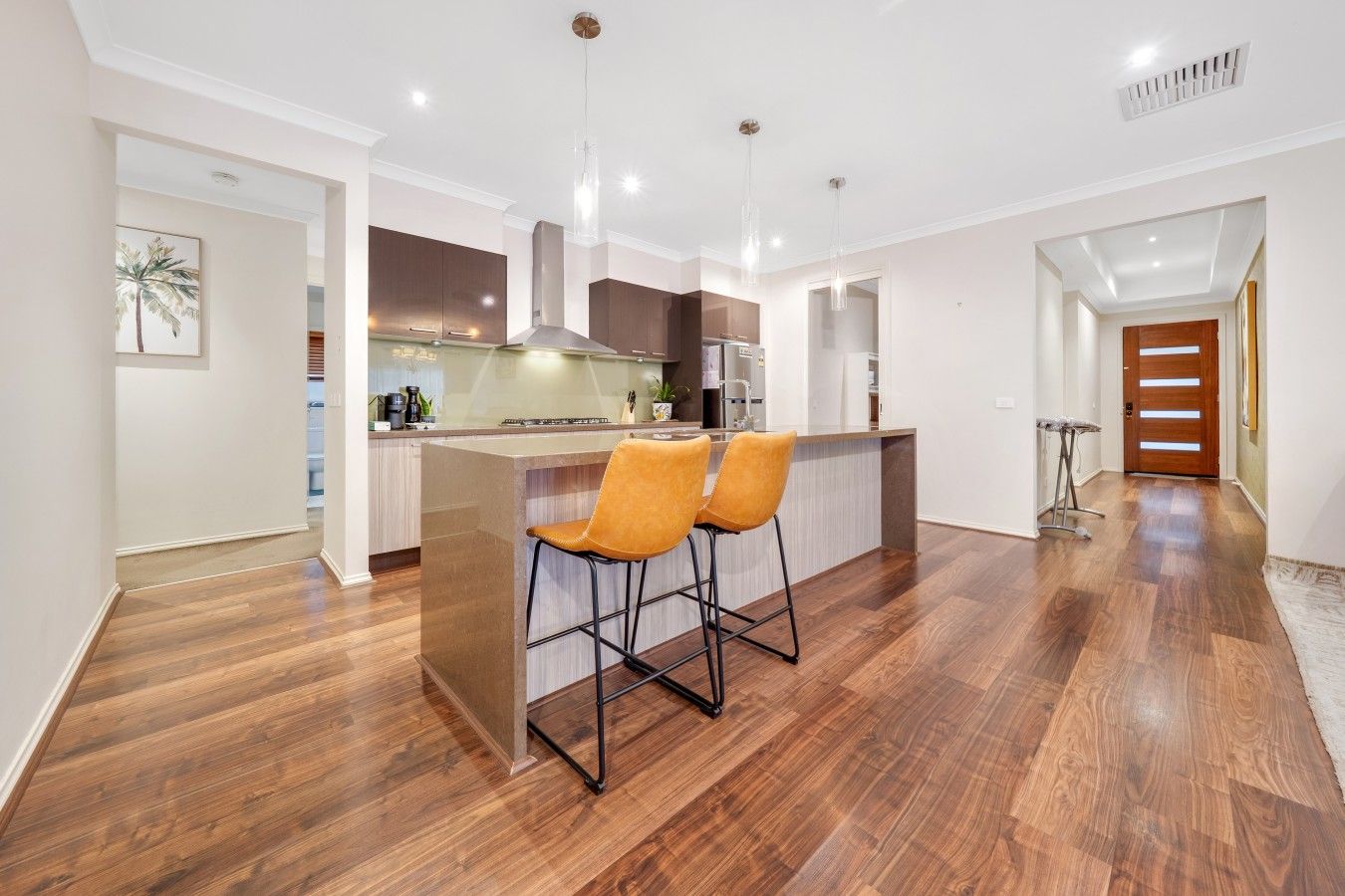 Une cuisine moderne avec un îlot central, des tabourets de bar et un plancher en bois.