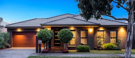 A modern two-story house with a garage, a well-lit front entrance, and a landscaped front yard.
