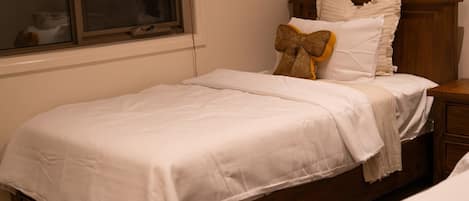 A single bed with a white bedspread, a decorative bow pillow, and a wooden headboard.