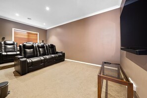 A home theater room with a reclining leather couch, a flat-screen TV, and a carpeted floor. - Spacious 4BR Family Retreat | Theatre & Sunroom (Berwick)