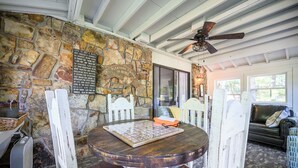 A stone wall, a wooden table with a chessboard, and a ceiling fan in a cozy room. - Mt.Fork Hideaway, Pickleball, Hot Tub, 4 private acres (Broken Bow)