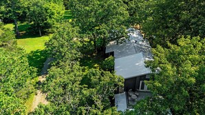 A house surrounded by dense forest, with a visible patio area and a clear sky. - Mt.Fork Hideaway, Pickleball, Hot Tub, 4 private acres (Broken Bow)
