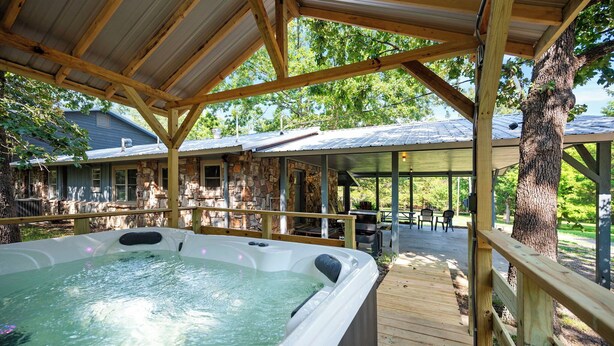 A hot tub under a wooden deck with stone walls and a covered patio area. - Mt.Fork Hideaway, Pickleball, Hot Tub, 4 private acres (Broken Bow)