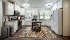 A modern kitchen with white cabinets, stainless steel appliances, and a patterned rug. - Mt.Fork Hideaway, Pickleball, Hot Tub, 4 private acres (Broken Bow)