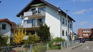 A two-story residential building with a balcony, a street view, and a clear sky.