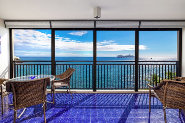 A balcony with a view of the ocean and a cruise ship.