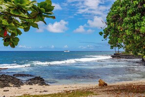 A beach with clear blue water, a boat in the distance, and rocky shores.
