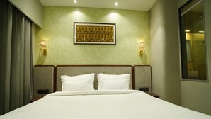 A hotel room with a large bed, two bedside lamps, a framed artwork on the wall, and a window on the right side. - PACHMARHI TIGER  (Pipariya)