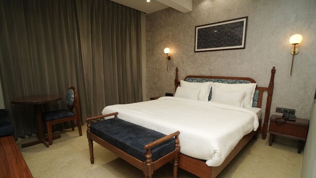A hotel room with a large bed, a bedside table, a chair, and a desk. - PACHMARHI TIGER  (Pipariya)