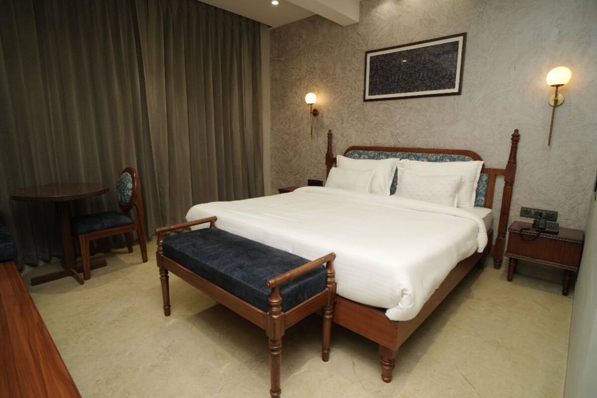 A hotel room with a large bed, a bedside table, a chair, and a desk.