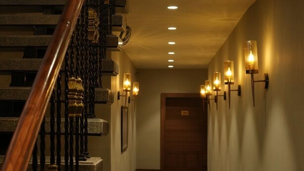 Un pasillo con escaleras de madera, alfombra estampada e iluminación en la pared.