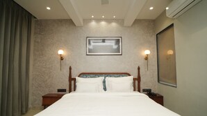 Una habitación de hotel con una cama grande, dos mesitas de noche, un cuadro colgado en la pared y una lámpara en el techo.