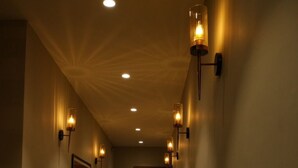 Un pasillo con alfombra estampada, luces en la pared y una puerta al final.