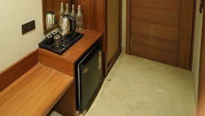 Una habitación compacta con un escritorio de madera, un refrigerador pequeño y un armario.