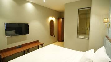 A hotel room with a bed, a TV mounted on the wall, a wooden bench, a mirror, and a shower area.