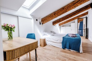 Cozy retreat with a sloped ceiling, featuring a comfortable bed and a stylish table with a vase of flowers.