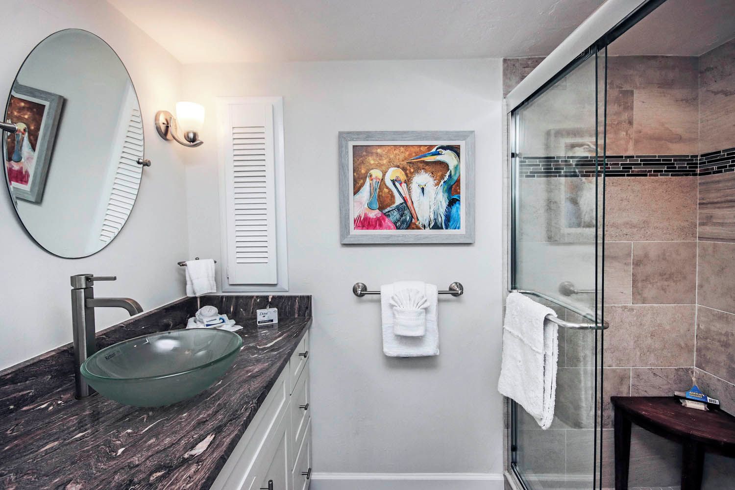Une salle de bain avec un lavabo en forme de bol en verre, un grand miroir, un tableau encadré et une cabine de douche en verre.