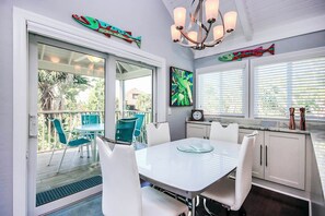 A modern kitchen with white cabinetry, a glass dining table, and teal chairs.