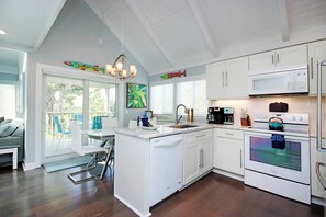 A modern kitchen with white cabinetry, a built-in island, stainless steel appliances, and a dining area with a view to the outdoors.