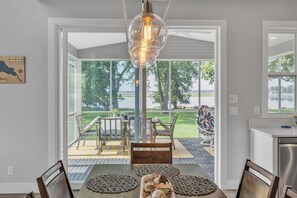 A dining area with a table set for four, a hanging light fixture, and a view of a patio with outdoor furniture. - Lakefront 4BR w/ Dock & Kayaks Oshkosh (Oshkosh)