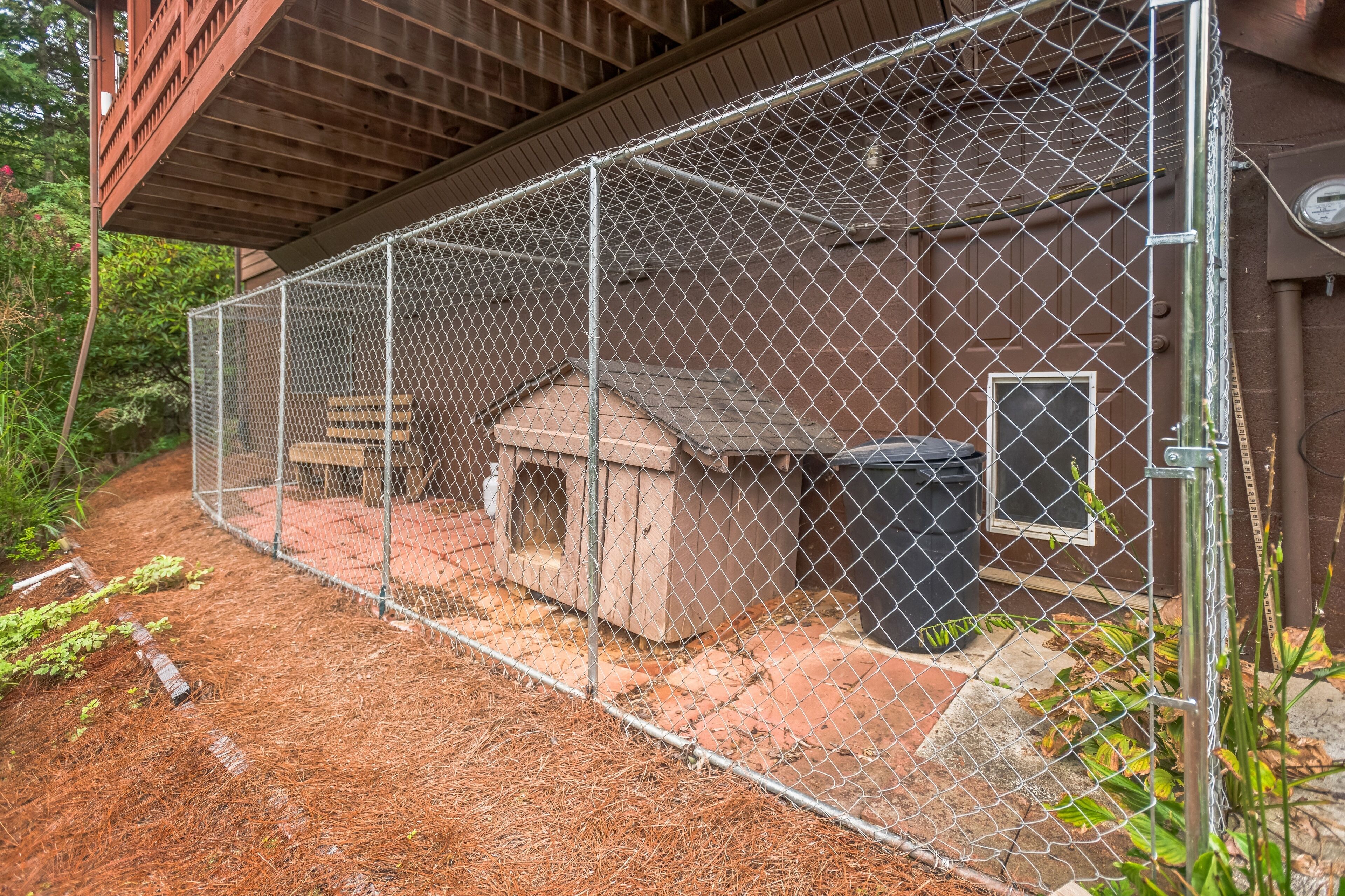 A fenced outdoor area with a wooden structure, possibly a barbecue or shed, and a trash bin.