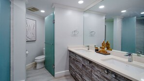 Un baño moderno con inodoro, una puerta verde, un espejo grande y un tocador de mármol.