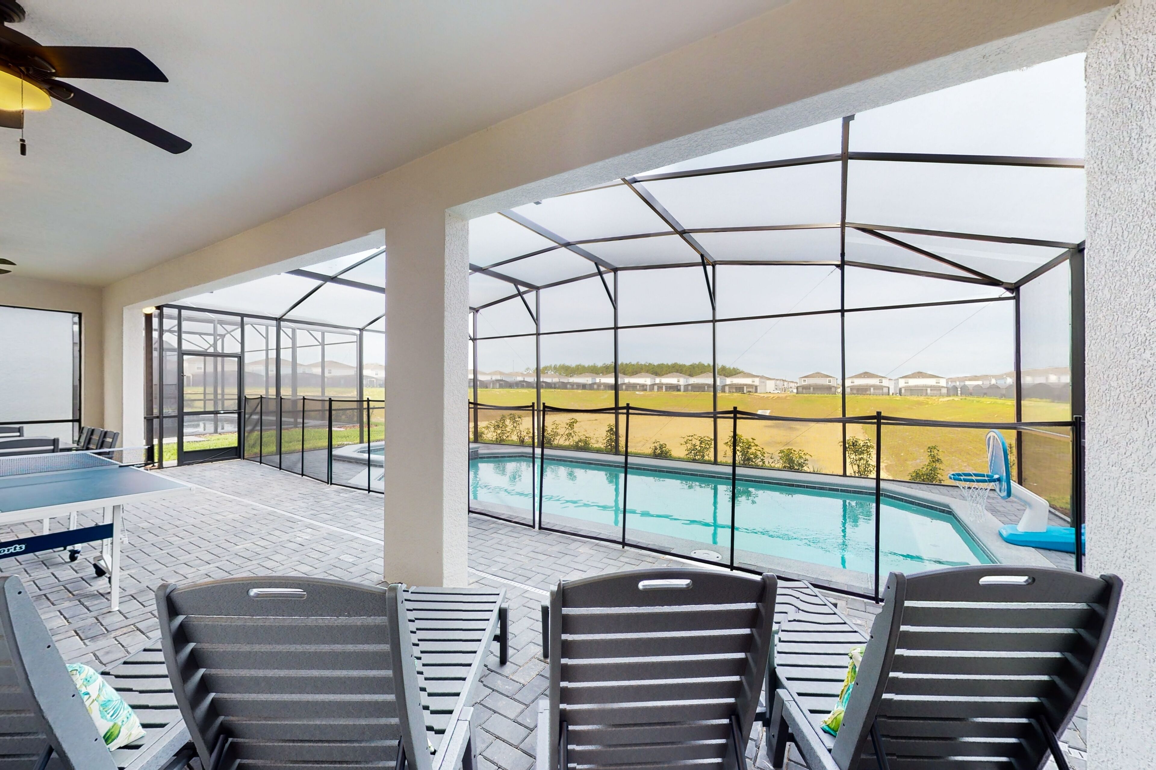 A covered outdoor area with a pool, lounge chairs, and a ping pong table.