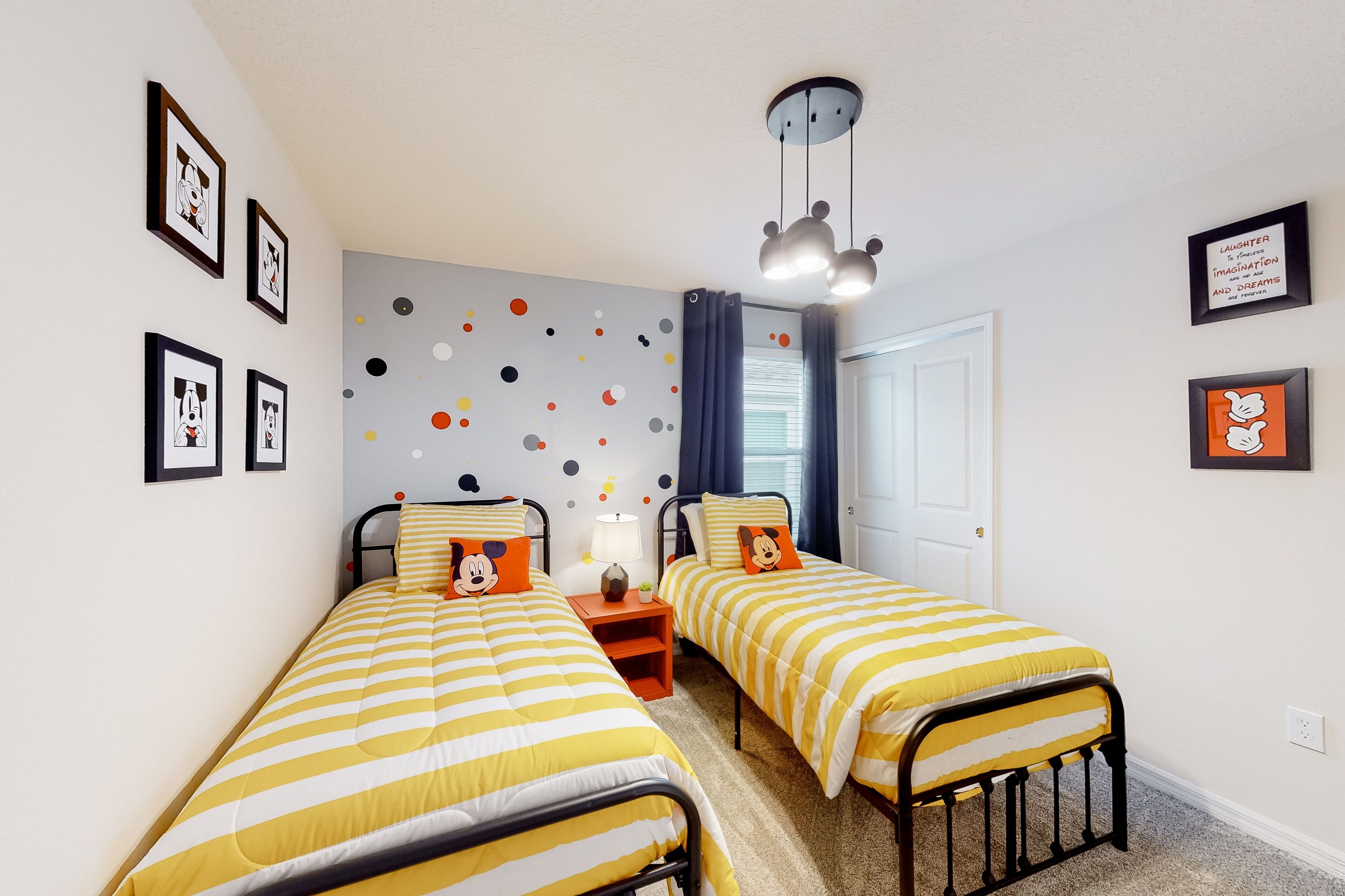 Ein Zimmer mit zwei Betten, jedes mit Mickey Mouse Kissen, einer Wand mit bunten Punkten und gerahmten Bildern.