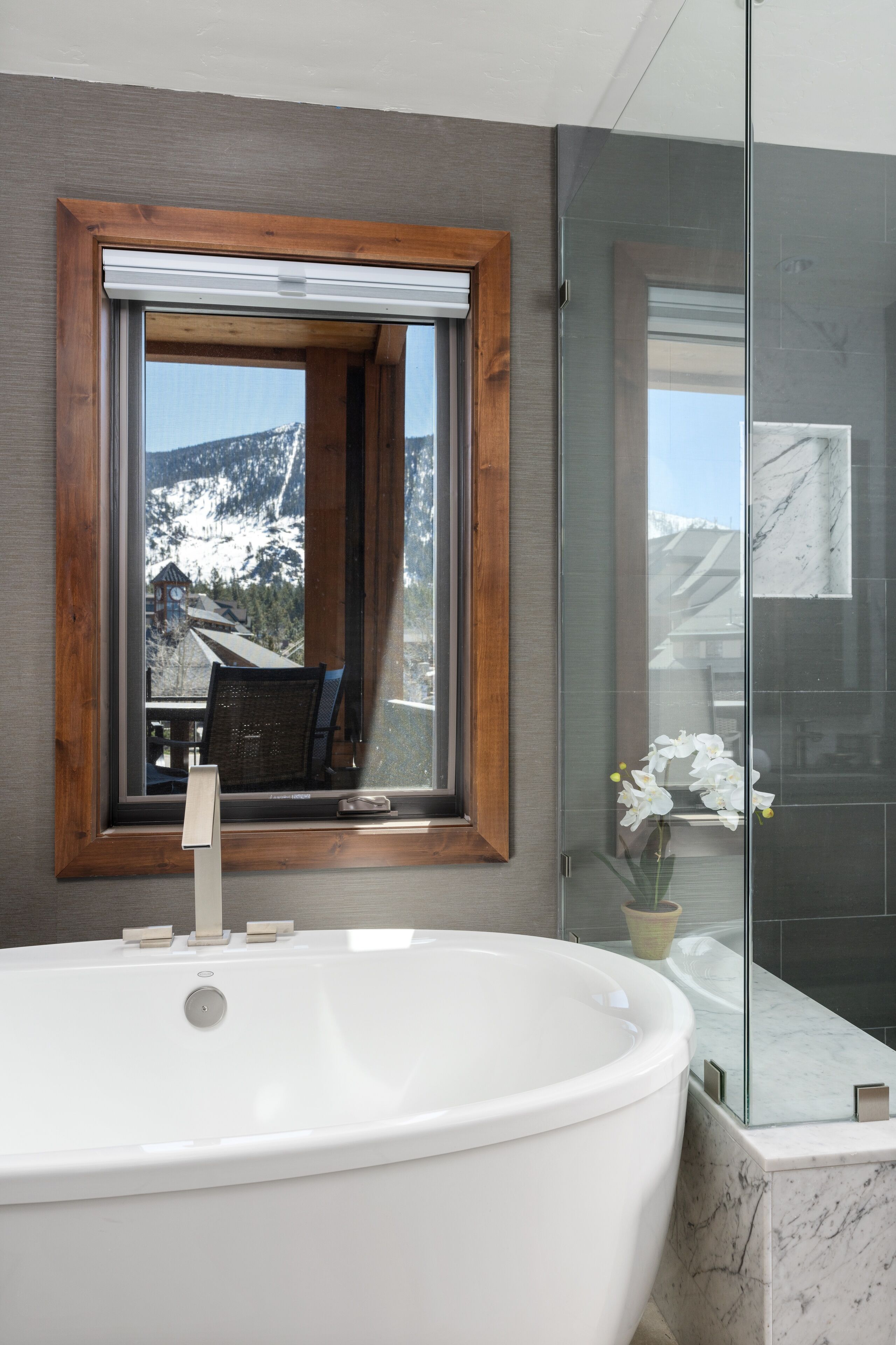 Une salle de bain avec une baignoire sur pieds, un miroir à cadre en bois et une cabine de douche en verre.