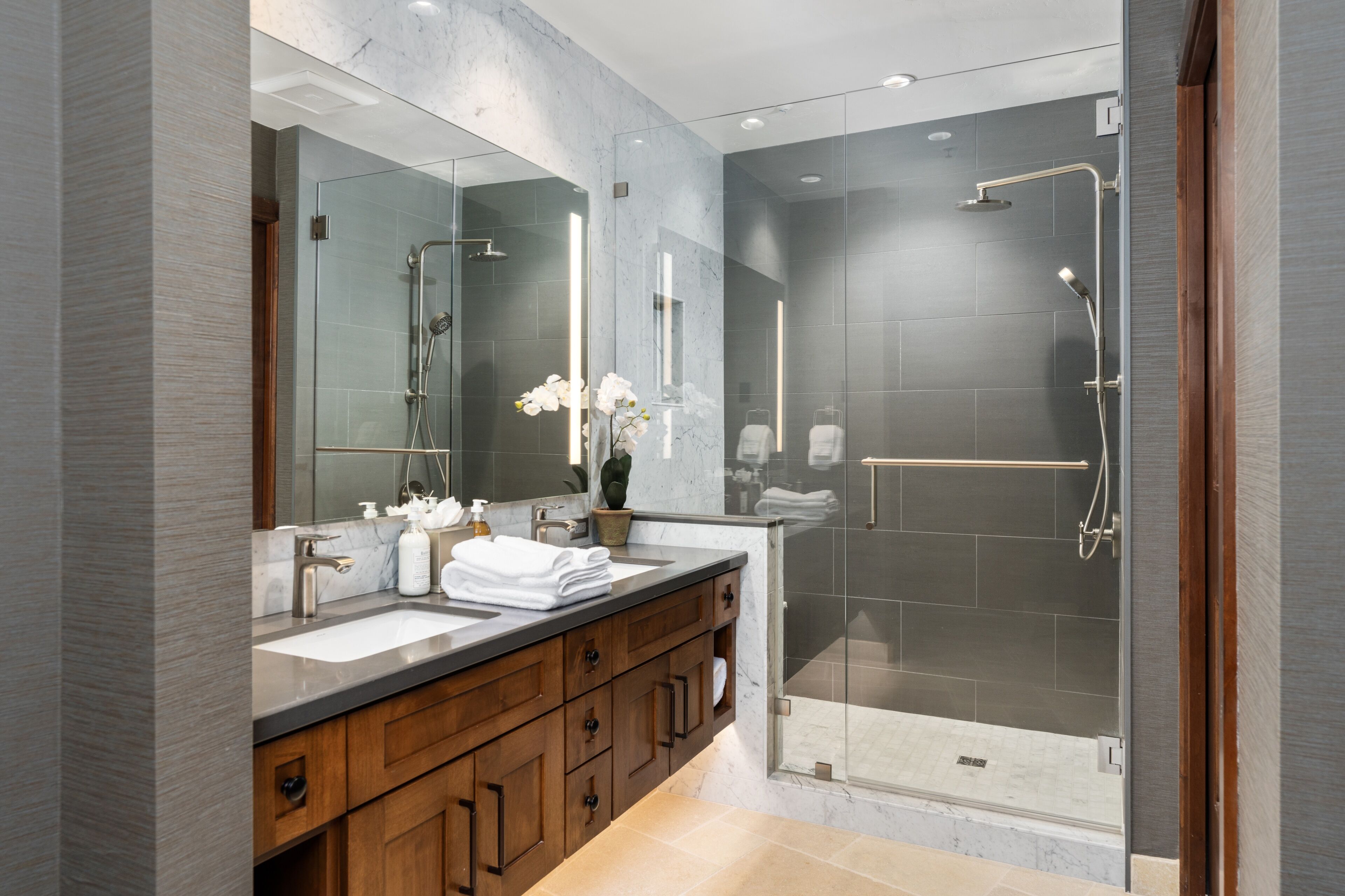 A modern bathroom with dual sinks, a large mirror, and a glass-enclosed shower area.