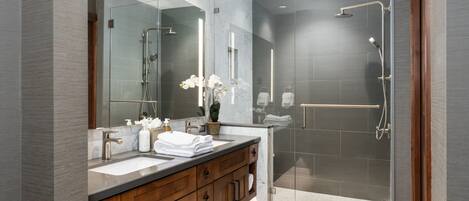 Un baño moderno con lavamanos dobles, un espejo grande y una zona de ducha con mampara de vidrio.