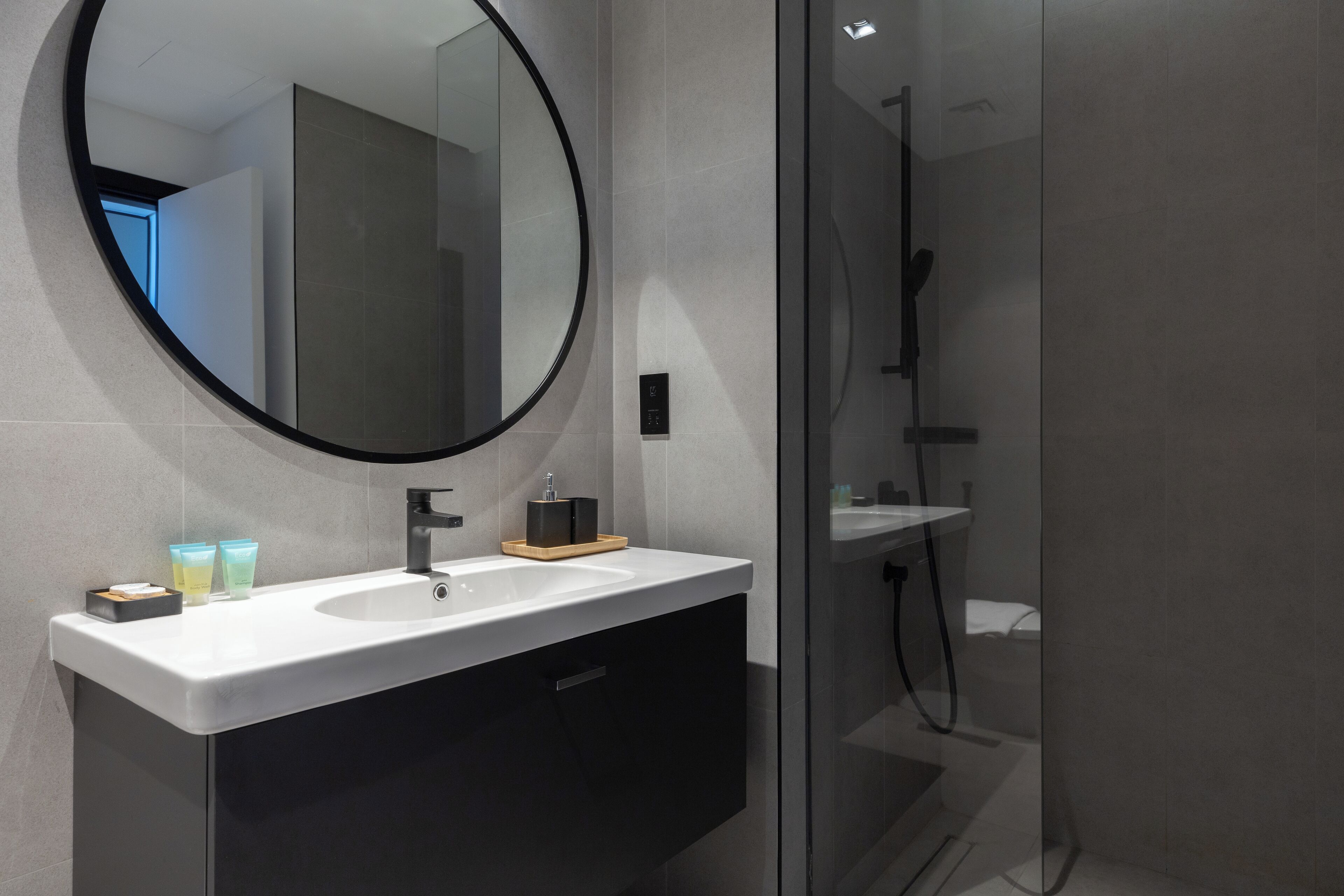 A modern bathroom with a round mirror, a white sink, and a glass shower enclosure.