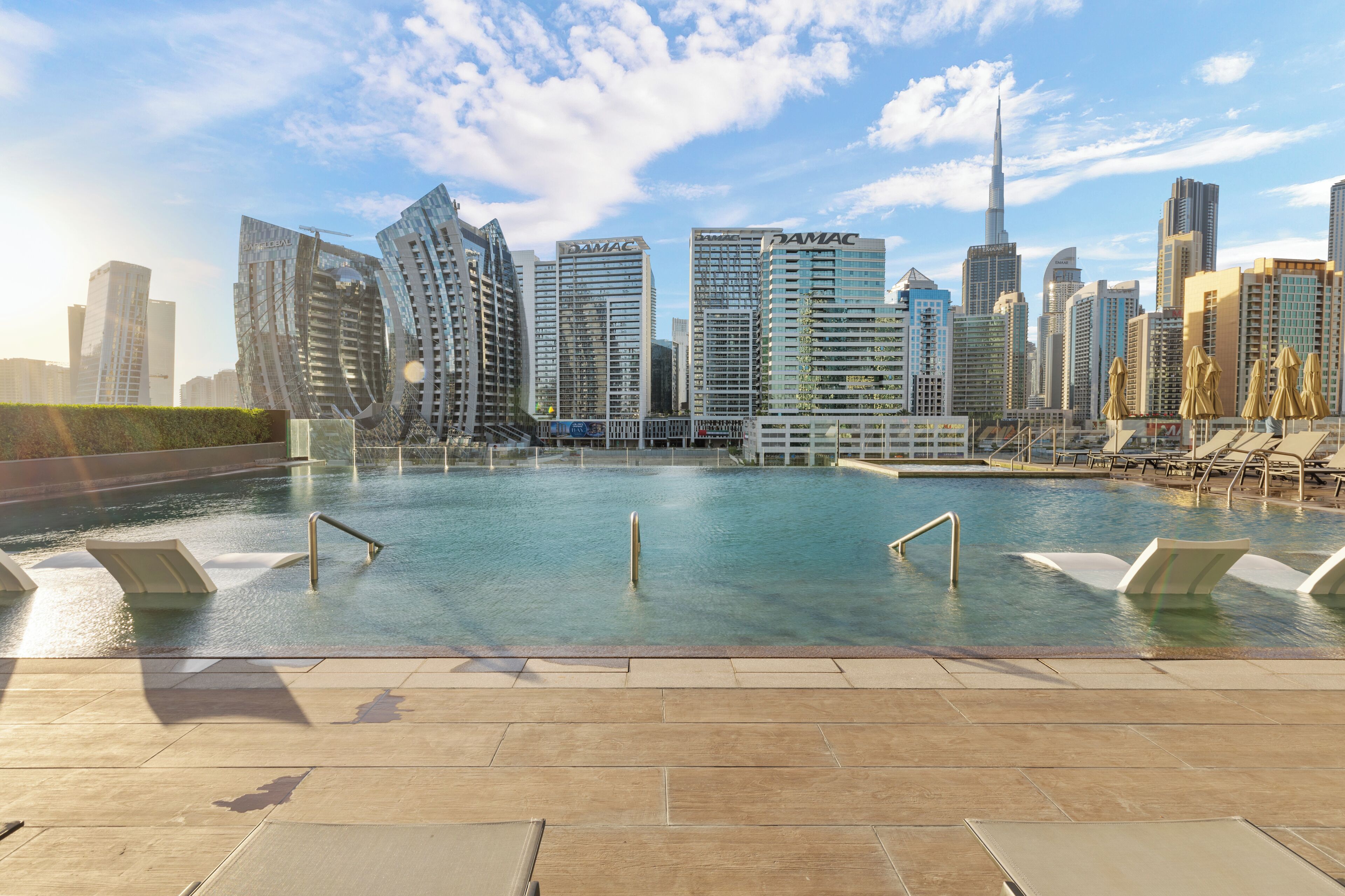 Une piscine dont l’arrière-plan offre une vue sur la ville, avec des bâtiments modernes et un gratte-ciel imposant.