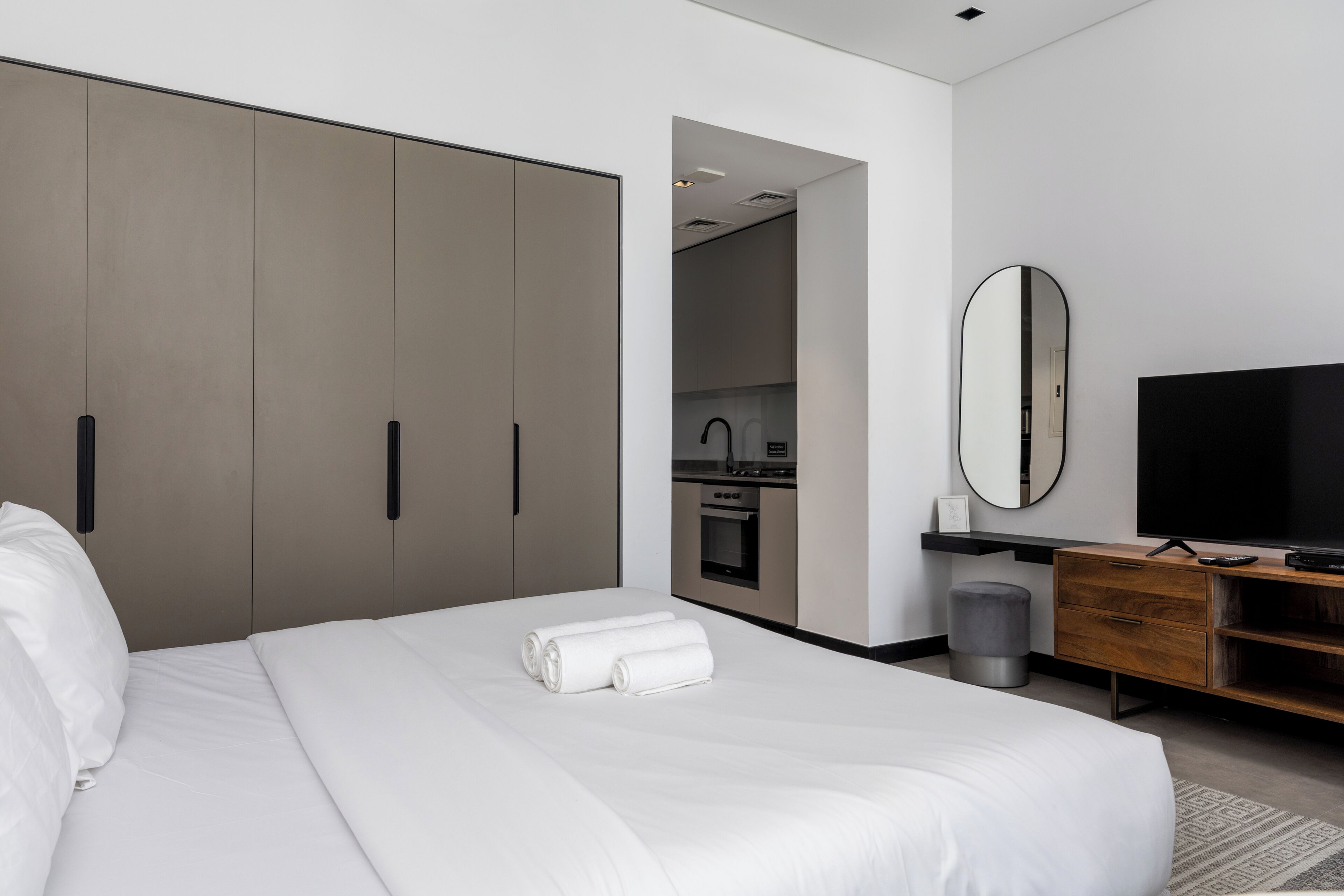 A modern hotel room with a large bed, a TV, a wardrobe, and a kitchenette.