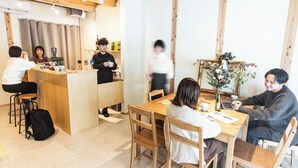 A cafe with wooden furniture, a counter, and a few patrons. - Fukuoka Guesthouse CAMP (Fukuoka)