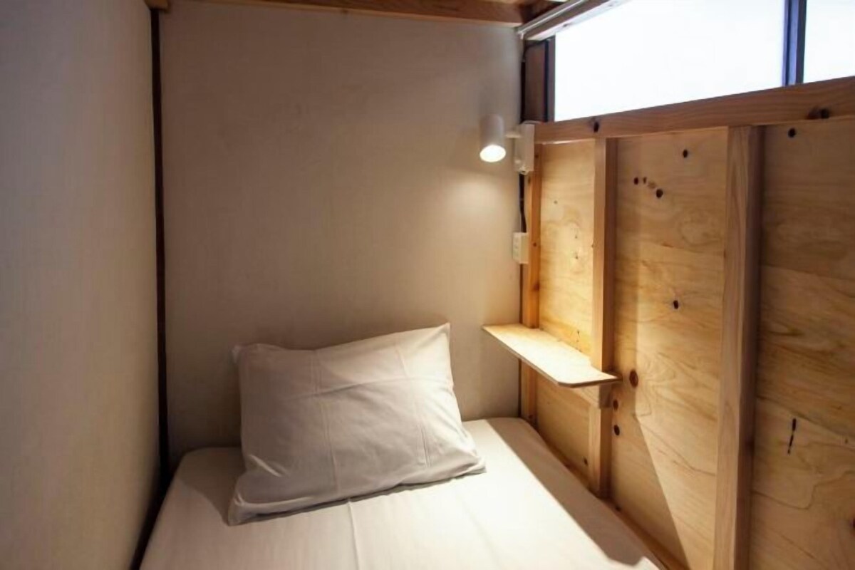Una habitación pequeña y acogedora con una cama individual, una almohada, una mesita de noche y una ventana con marco de madera.