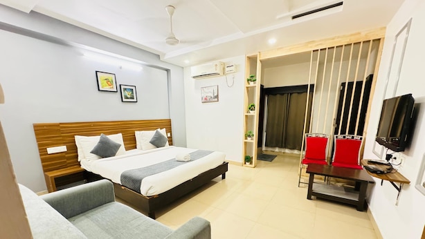 A hotel room with a bed, a sofa, a TV, a desk, and a balcony with curtains. - Bommarillu Residency (Hyderabad)