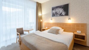 Quarto de hotel com uma cama grande, uma cadeira, uma mesinha e um quadro pendurado na parede.