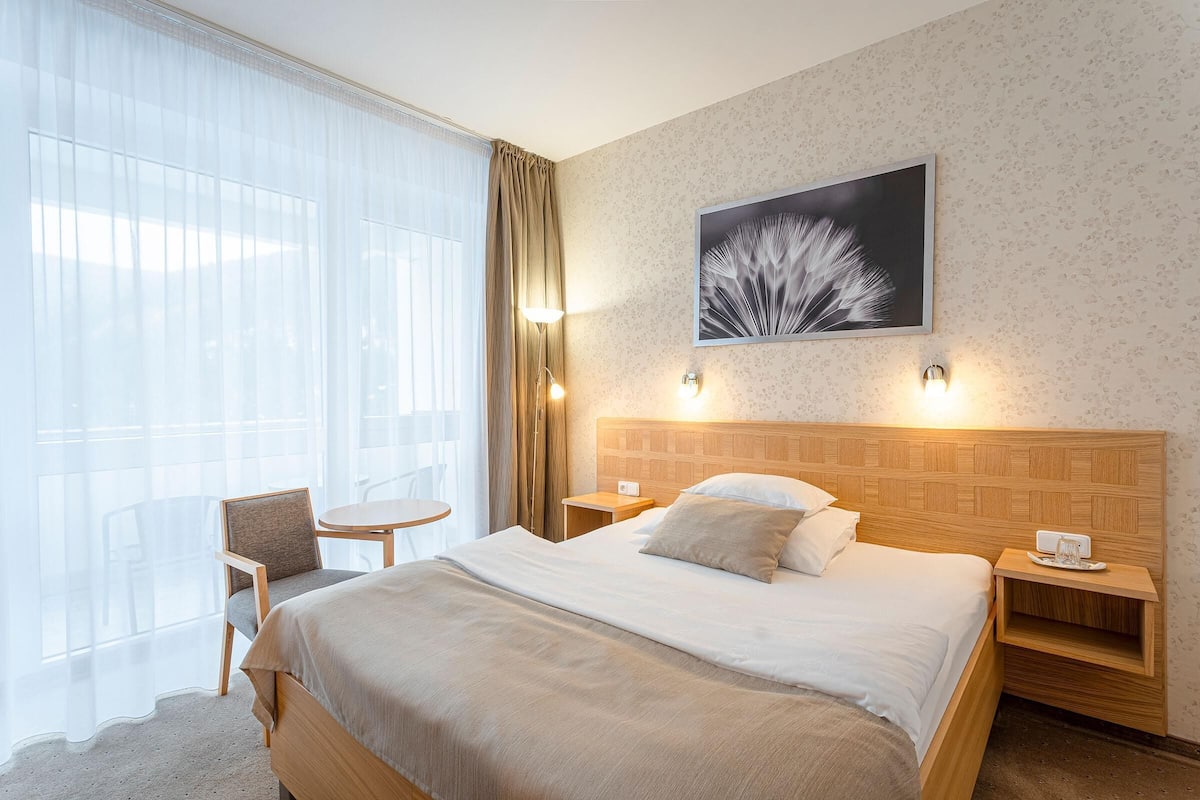 Ein Hotelzimmer mit einem großen Bett, einem Sessel, einem kleinen Tisch und einem an der Wand hängenden Bild.