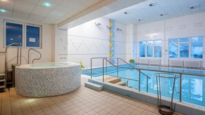 Piscina interior moderna com hidromassagem, paredes de vidro transparente e chão em mosaico.